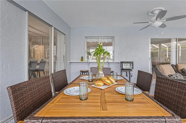 Covered patio featuring a wood-finish dining table and woven seating, a ceiling fan, sliding glass doors, and a pass-through window