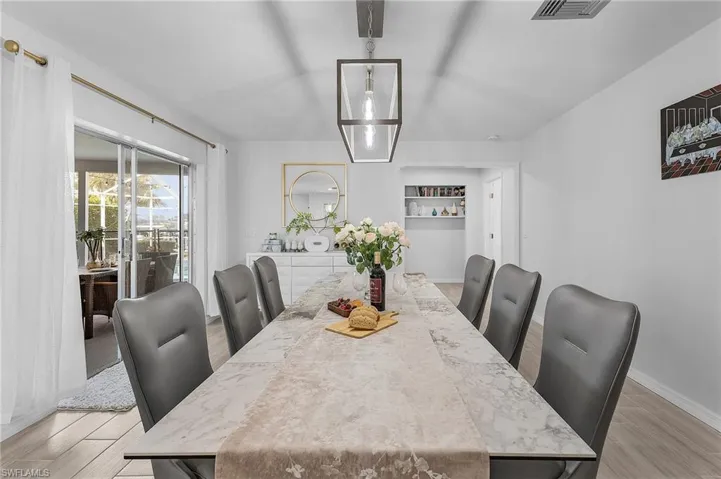 Open-concept dining area featuring a rectangular table with a stone-finish top, an overhead linear pendant light fixture, and wood-finish flooring