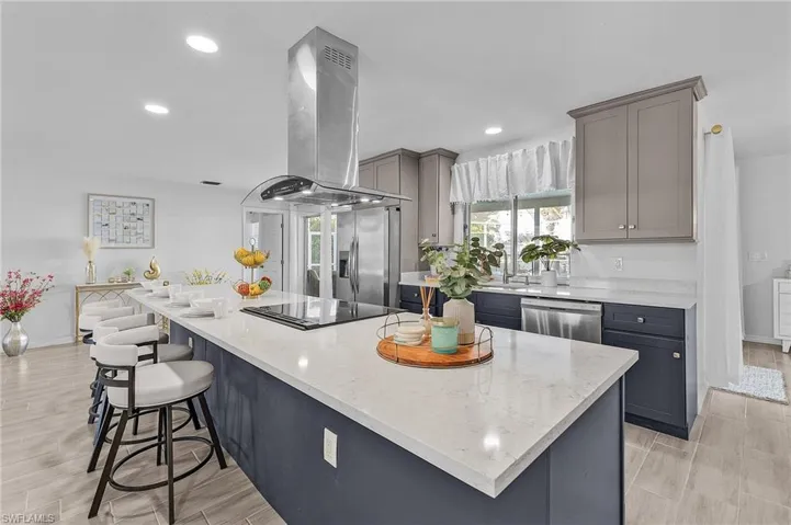 Spacious kitchen featuring a large island with seating, a smooth cooktop with a stainless steel range hood, stainless steel appliances, recessed lighting, and wood-finish flooring