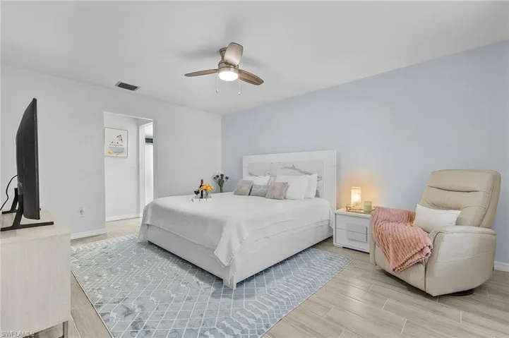 Spacious bedroom featuring wood-finish tile flooring, a contemporary ceiling fan with integrated lighting, and a light-colored accent wall