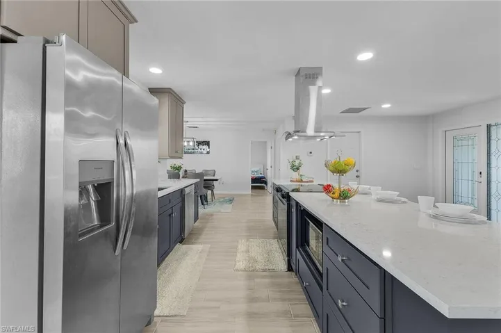 Gourmet kitchen featuring a large island with white stone countertops, dark blue cabinetry, and stainless steel appliances including a refrigerator and range hood