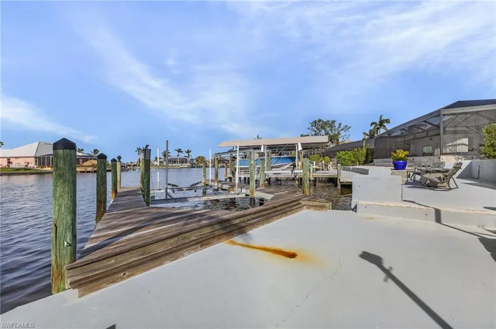 Waterfront property featuring a private wooden dock, concrete patio, boat lift, and screened outdoor area