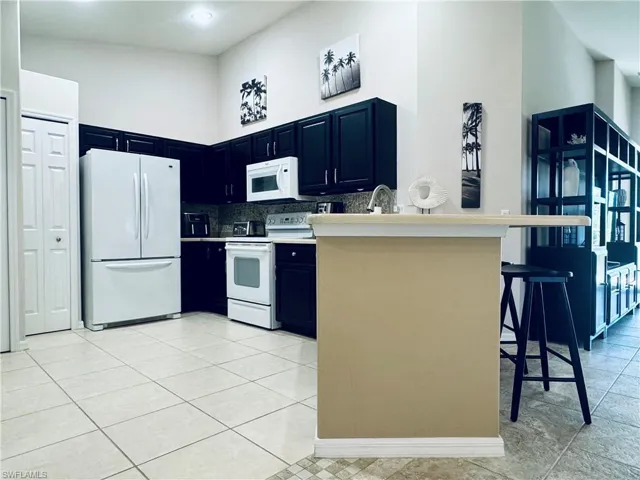 Kitchen featuring white appliances, a breakfast bar, blue cabinetry, a high ceiling, and a sink