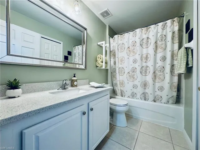 Bathroom featuring tile patterned flooring, visible vents, toilet, shower / bath combo, and vanity