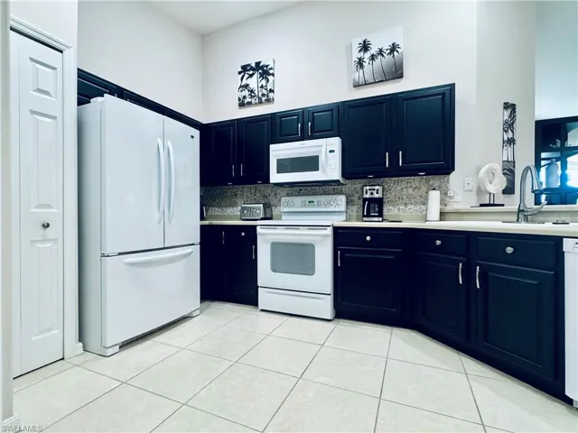 Kitchen with blue cabinetry, white appliances, light countertops, and a sink