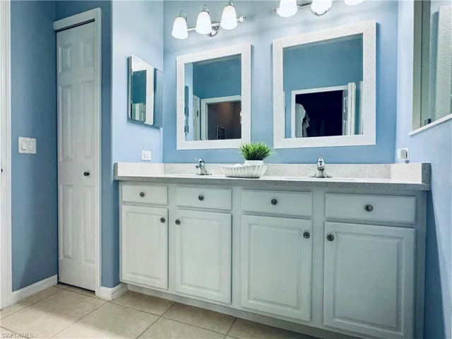 Full bath with tile patterned floors, baseboards, double vanity, and a sink