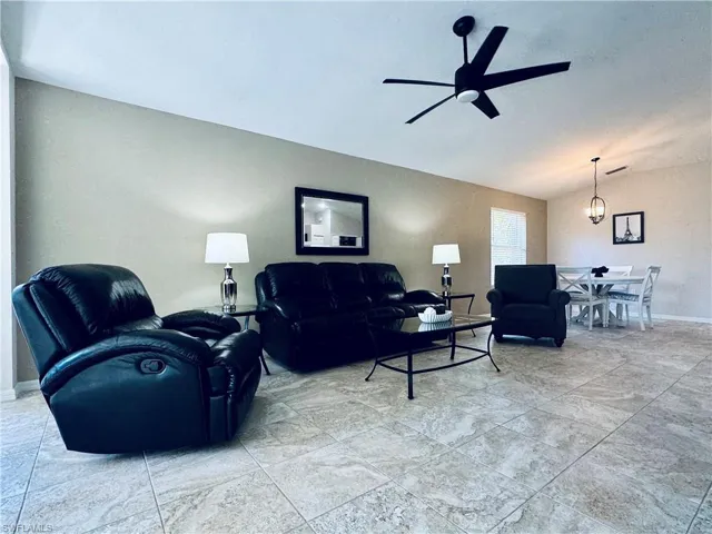 Living room featuring baseboards, ceiling fan with notable chandelier, and vaulted ceiling