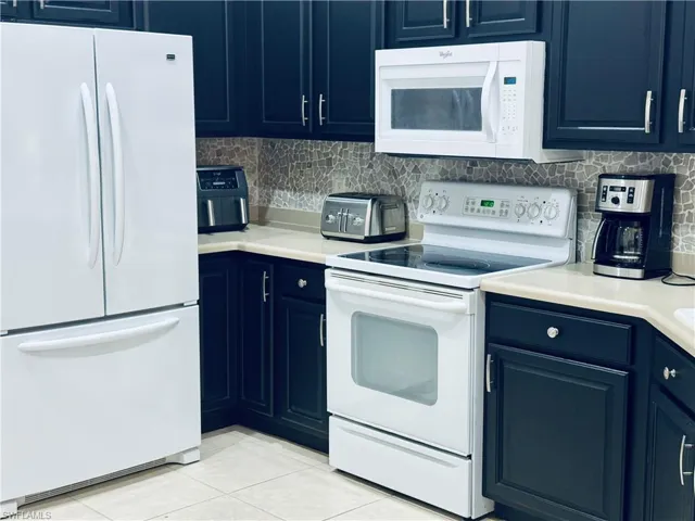 Kitchen with white appliances, light tile patterned flooring, light countertops, blue cabinets, and backsplash