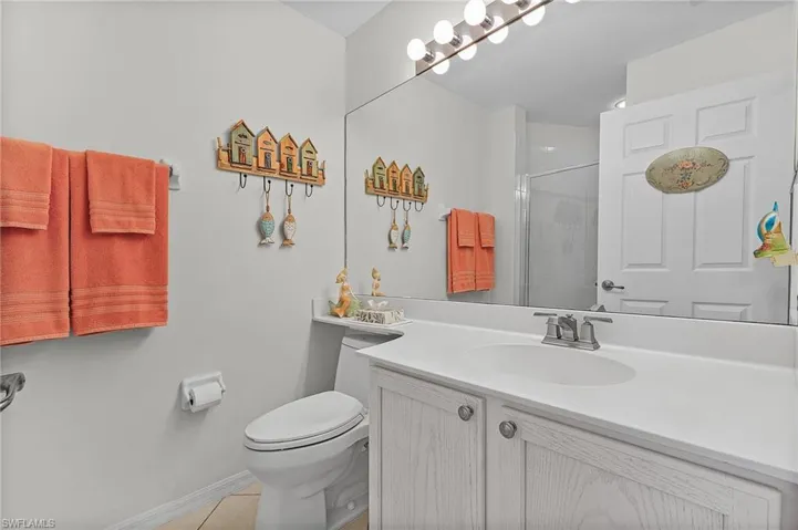 Bathroom with an enclosed shower, vanity, tile patterned floors, and toilet