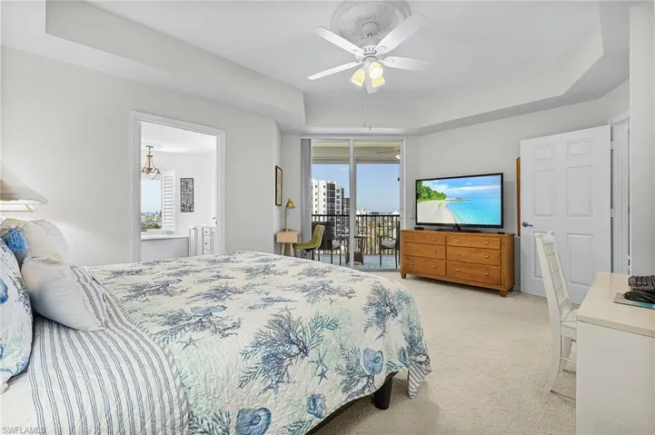Carpeted bedroom featuring ceiling fan, a tray ceiling, access to exterior, and ensuite bath