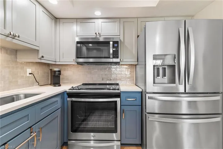 Kitchen with blue cabinets, appliances with stainless steel finishes, and tasteful backsplash