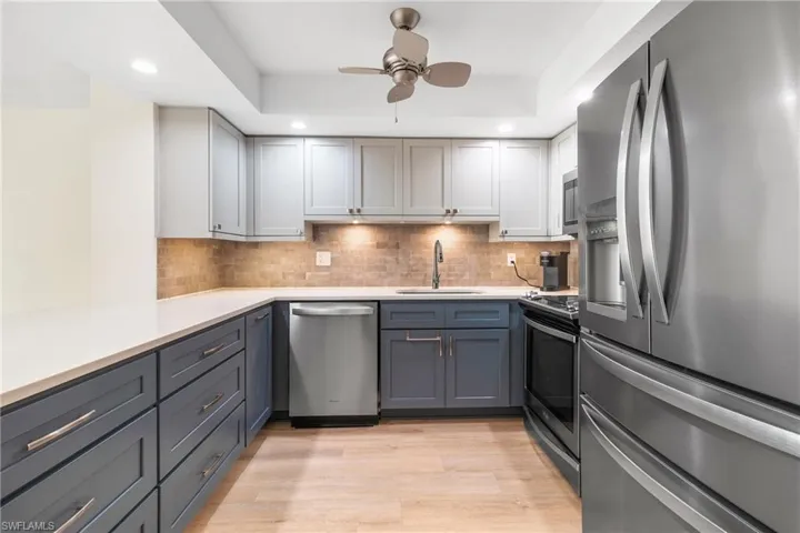 Kitchen with gray cabinetry, ceiling fan, sink, stainless steel appliances, and tasteful backsplash