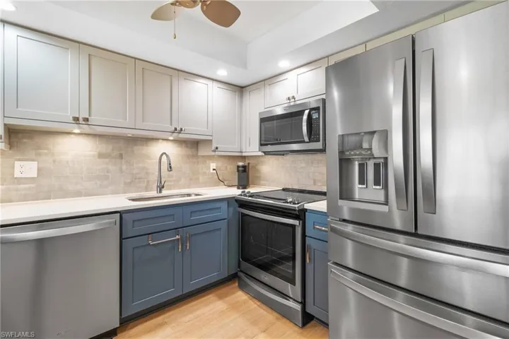 Kitchen featuring appliances with stainless steel finishes, backsplash, ceiling fan, sink, and light hardwood / wood-style flooring