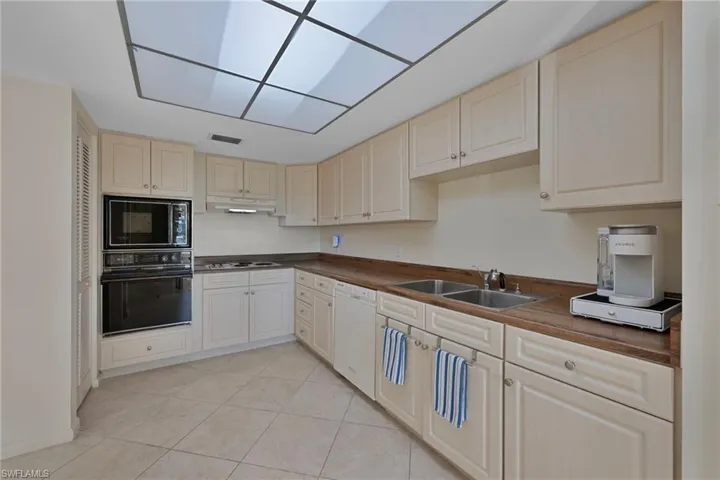 Kitchen featuring black appliances, light tile patterned flooring, cream cabinets, and under cabinet range hood