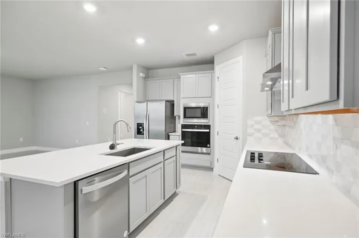 Kitchen featuring stainless steel appliances, a sink, light countertops, a center island with sink, and recessed lighting