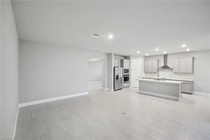 Kitchen with stainless steel appliances, wall chimney exhaust hood, tasteful backsplash, gray cabinetry, and recessed lighting