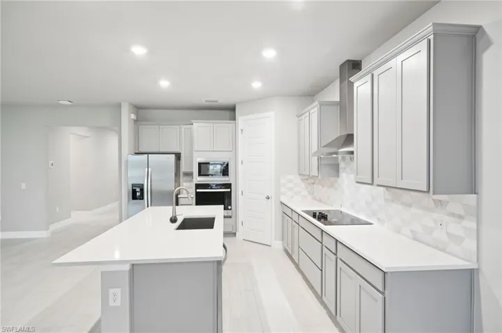 Kitchen with stainless steel appliances, a sink, wall chimney exhaust hood, gray cabinetry, and recessed lighting