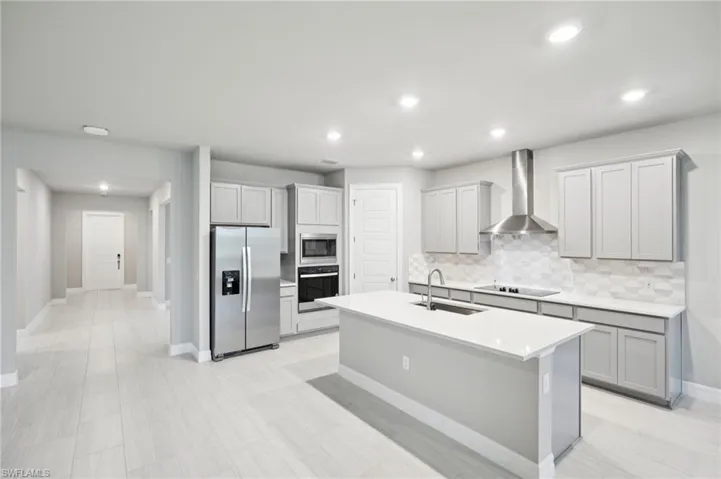Kitchen featuring black appliances, wall chimney range hood, a sink, an island with sink, and decorative backsplash