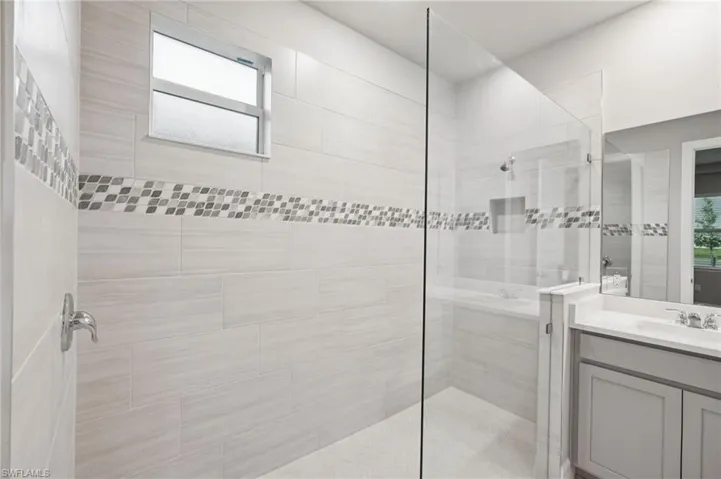 Bathroom featuring a tile shower, vanity, and plenty of natural light