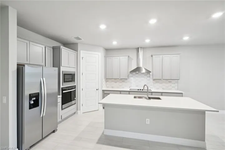 Kitchen featuring stainless steel appliances, wall chimney range hood, a sink, tasteful backsplash, and a kitchen island with sink