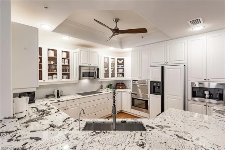 Kitchen featuring a tray ceiling, white cabinets, appliances with stainless steel finishes, recessed lighting, and light stone counters