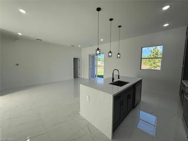 Kitchen featuring open floor plan, light stone counters, pendant lighting, dark cabinetry, and recessed lighting