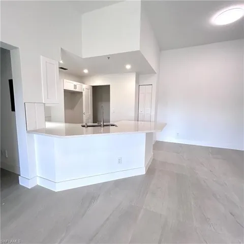 Kitchen featuring baseboards, a peninsula, a towering ceiling, white cabinets, and a sink