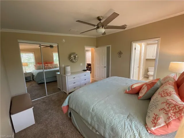 Carpeted bedroom with a closet, ensuite bath, ceiling fan, and crown molding