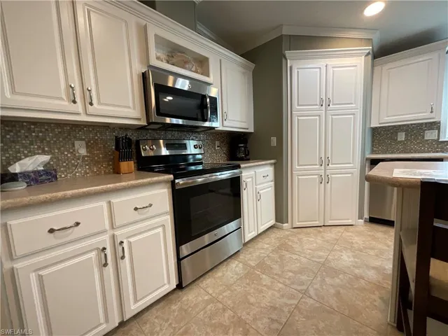 Kitchen with white cabinets, decorative backsplash, stainless steel appliances, and crown molding