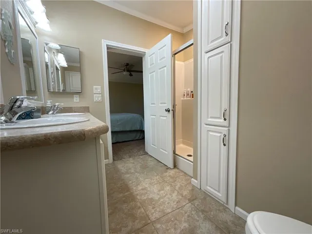 Bathroom with ceiling fan, toilet, a shower with door, vanity, and ornamental molding