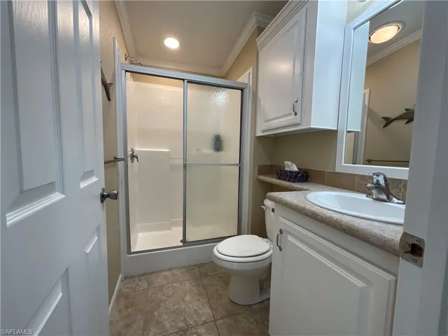 Bathroom with tile patterned floors, ornamental molding, vanity, a shower with door, and toilet