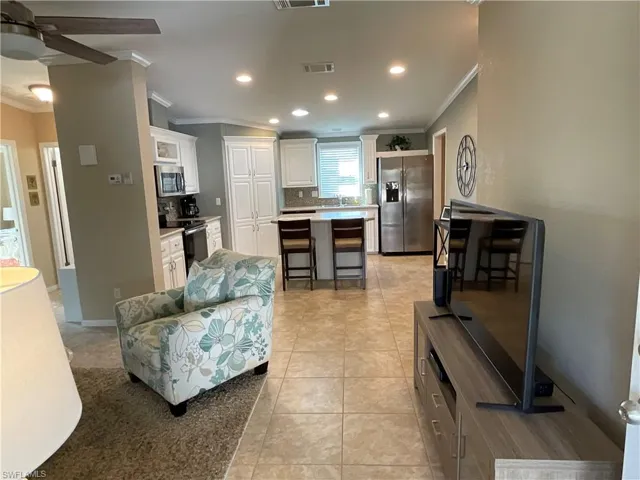Living room with ceiling fan, light tile patterned floors, and crown molding