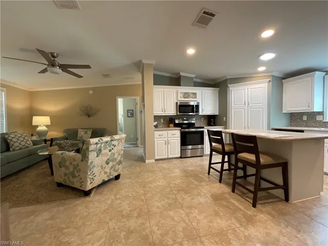 Kitchen with white cabinets, a kitchen breakfast bar, ornamental molding, and appliances with stainless steel finishes