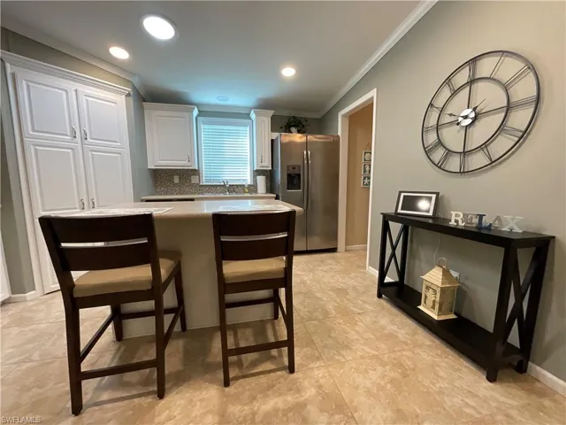 Kitchen with white cabinetry, backsplash, stainless steel fridge, a breakfast bar area, and ornamental molding