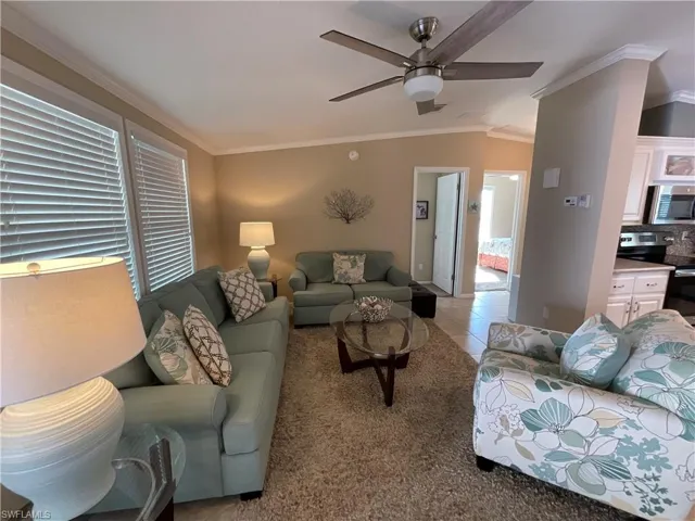 Living room featuring crown molding, light tile patterned floors, ceiling fan, and lofted ceiling