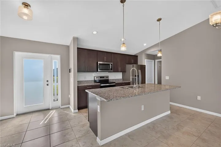 Kitchen featuring a granite-topped island, dark wood-finish cabinetry, stainless steel appliances, and a tile backsplash