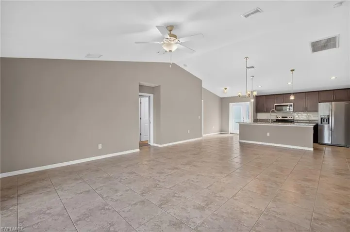 Vaulted ceilings, tile flooring, kitchen island with pendant lighting, stainless steel appliances, and dark wood-finish cabinetry