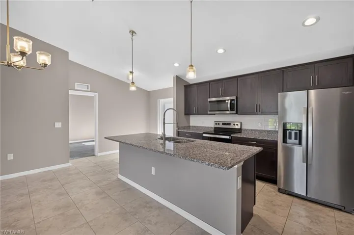 Kitchen featuring dark wood-finish cabinetry, stainless steel appliances, granite countertops, and tile flooring