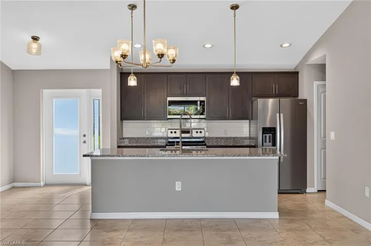 Kitchen island with granite countertop, dark wood-finish cabinetry, stainless steel appliances, tile backsplash, and tile flooring
