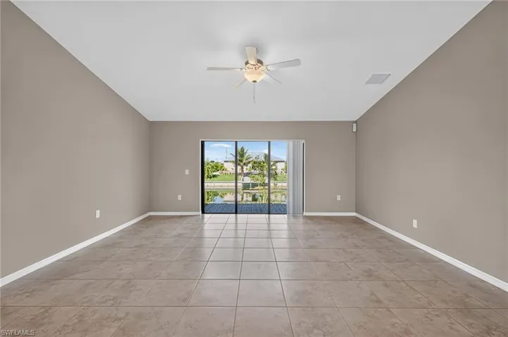 Tiled flooring with neutral wall tones, featuring a ceiling fan, and sliding glass doors that open to a water channel