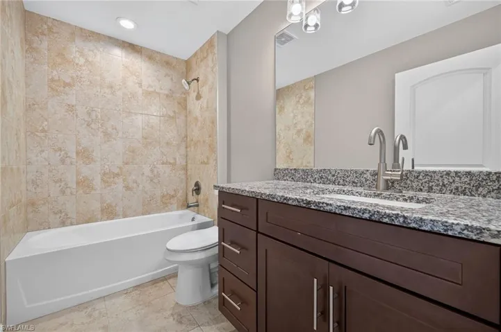 Granite countertop, wood-finish vanity, undermount sink, ceramic tile flooring, and tiled shower surround