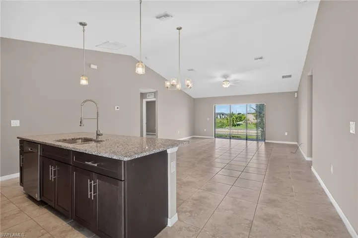 Kitchen island with granite-style countertop, stainless steel sink, and pendant lighting