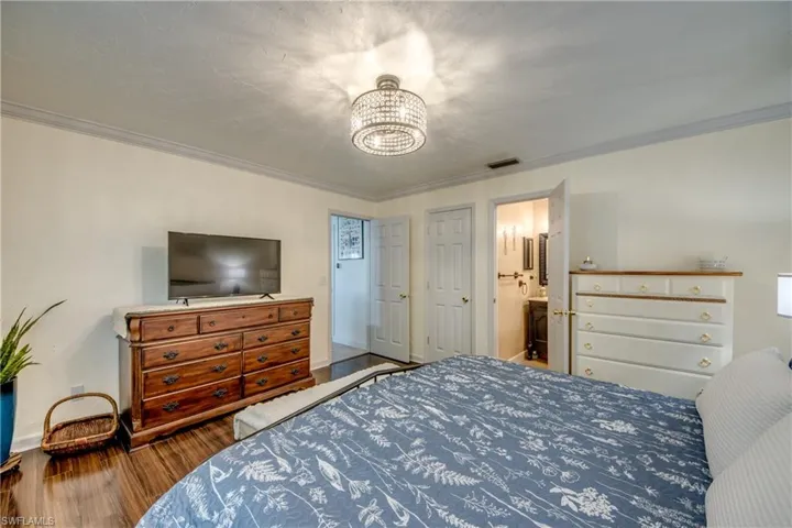 Bedroom featuring ornamental molding, wood finished floors, connected bathroom, and hanging lights