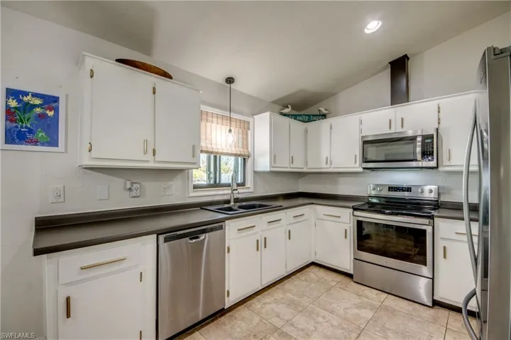 Kitchen featuring stainless steel appliances, lofted ceiling, decorative light fixtures, white cabinetry, and dark countertops
