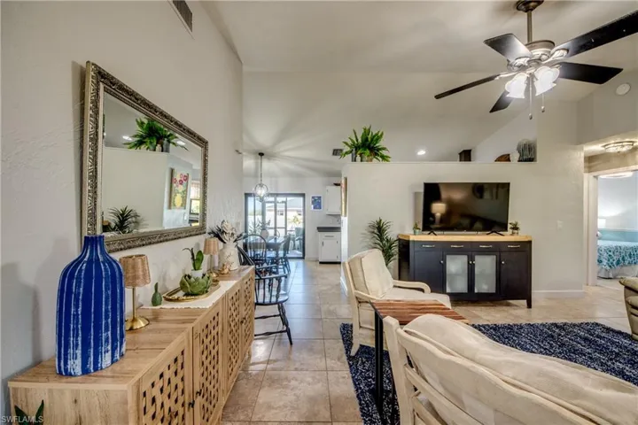 Living area with vaulted ceiling, a ceiling fan, and light tile patterned floors