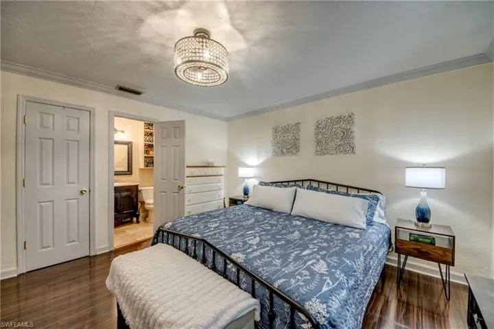 Bedroom featuring crown molding, dark wood finished floors, ensuite bathroom, and suspended lighting