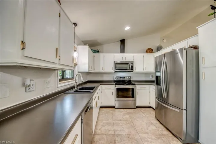 Kitchen with stainless steel appliances, lofted ceiling, hanging light fixtures, white cabinets, and dark countertops