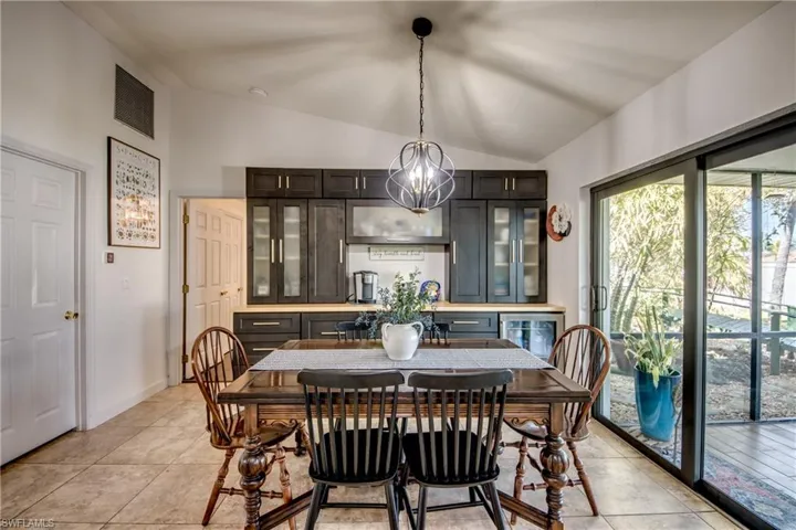 Dining area with lofted ceiling, wine cooler, hanging lights, and light tile patterned floors