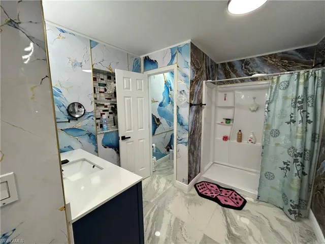 Full bath with vanity, stone wall, a stall shower, and light marble finish floors