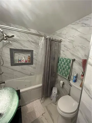 Full bath featuring marble finish floors, tile walls, and shower / bath combo